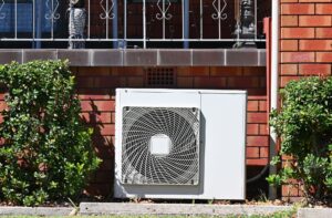 Air conditioning unit installed outside a brick wall, surrounded by greenery, relevant to HVAC maintenance and comfort in Woods Cross.