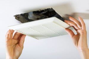 Hands removing an air conditioning vent cover from the ceiling, illustrating HVAC maintenance and troubleshooting tips for homeowners in Woods Cross.